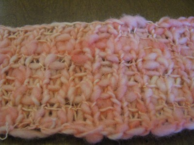 Close up of pink spun yarn knitted into scarf.